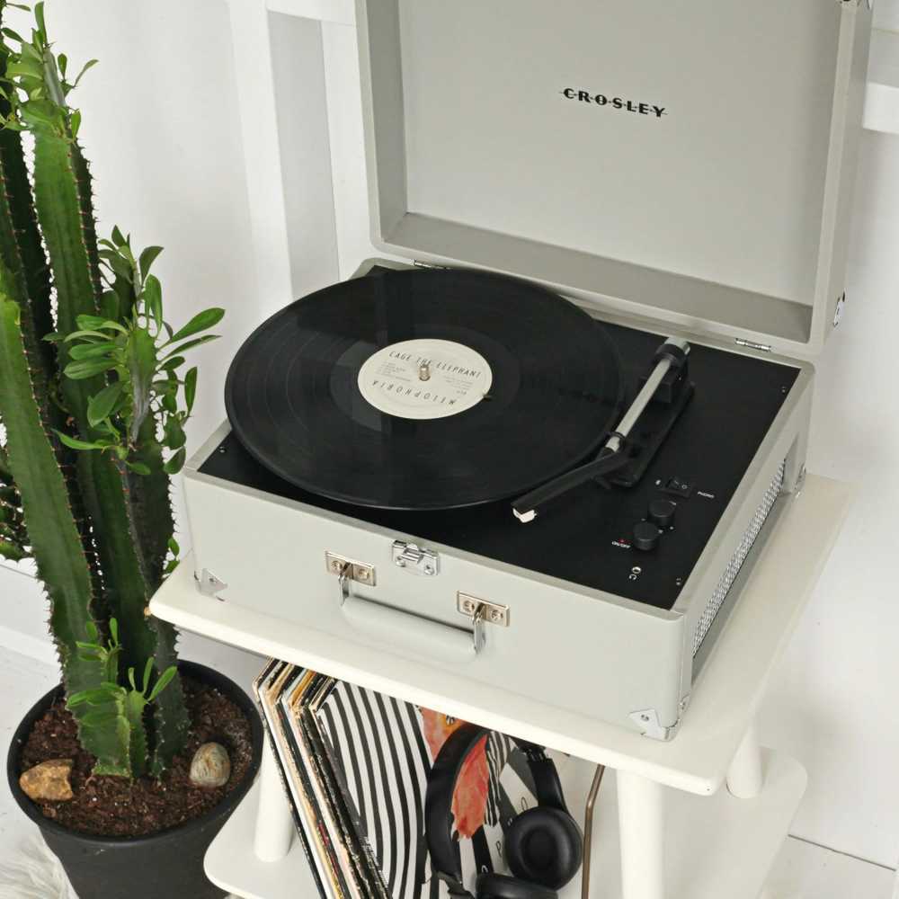 Crosley Anthology Portable Turntable - Gray with a black vinyl record playing, positioned near a cactus plant and records stored underneath the shelf