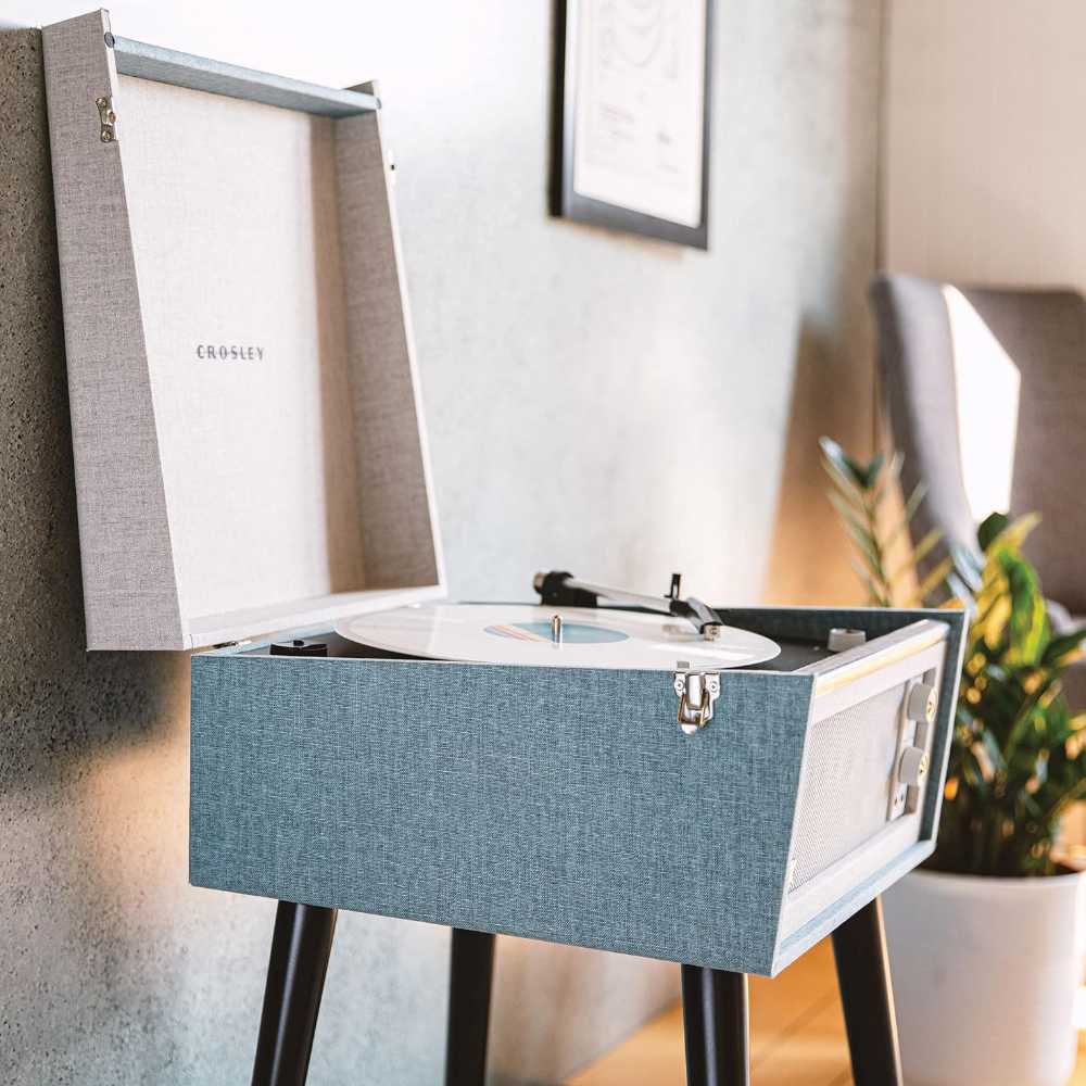 Crosley Bermuda Portable Turntable with Bluetooth InOut - Tourmaline is shown open, playing a vinyl record on a black stand in a cozy living room setup