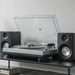 Crosley K100A Record Player with S100 Speakers - Silver sits on a modern black shelf, emphasizing its aluminum platter and black speakers