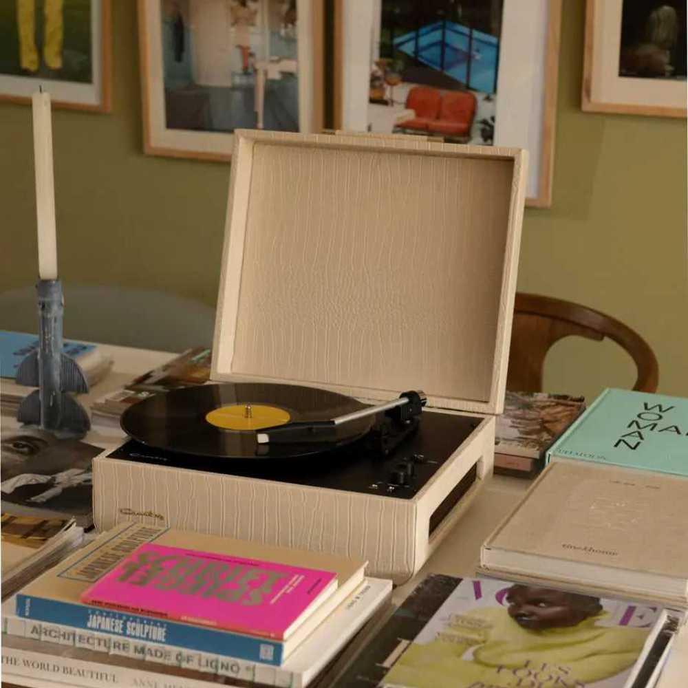 Crosley Mercury Portable Turntable - Cream Croc is shown playing a vinyl record on a stylish table surrounded by magazines and decor