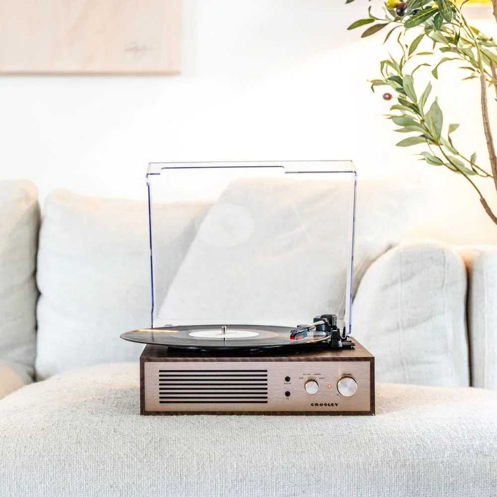 Crosley Miles Record Player - Walnut rests on a cozy beige couch, blending perfectly with a modern home aesthetic while spinning a vinyl