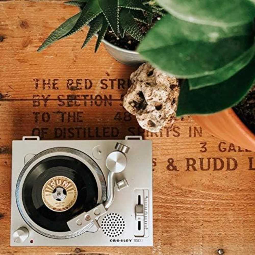 Crosley RSD3 Mini Turntable for 3 Inch Vinyl Records w Johnny Cash Single is shown on a rustic surface surrounded by plants