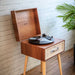 Crosley Rohe Turntable - Natural is positioned near a white brick wall, featuring a vinyl record on the turntable ready to play