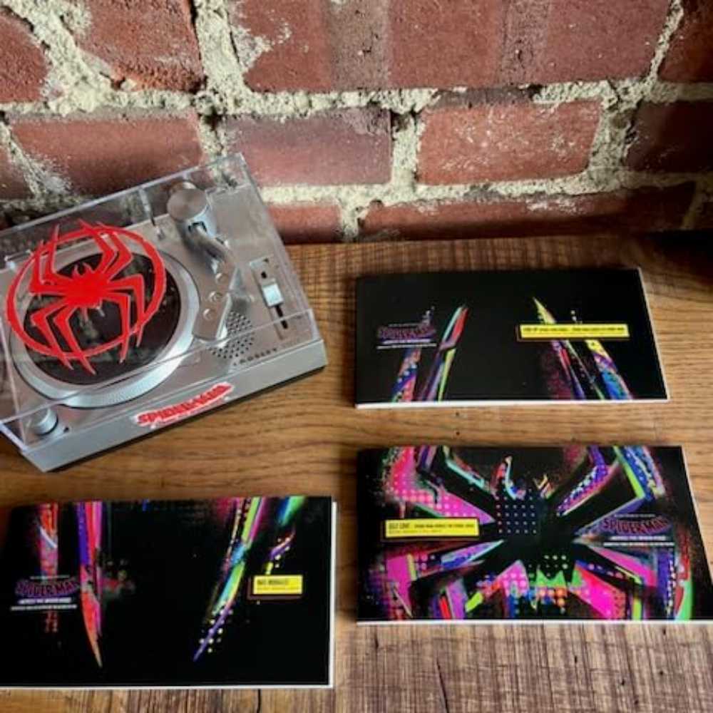 Crosley Spider-Man RSD3 Mini Turntable with 3 inch Releases next to three vinyl sleeves with colorful abstract designs on a wooden surface