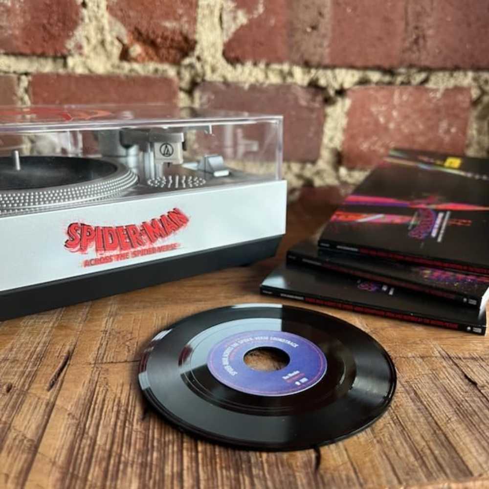 Crosley Spider-Man RSD3 Mini Turntable with 3 inch Releases on a wooden surface, with a vinyl record and additional sleeves featuring the Spider-Man logo nearby