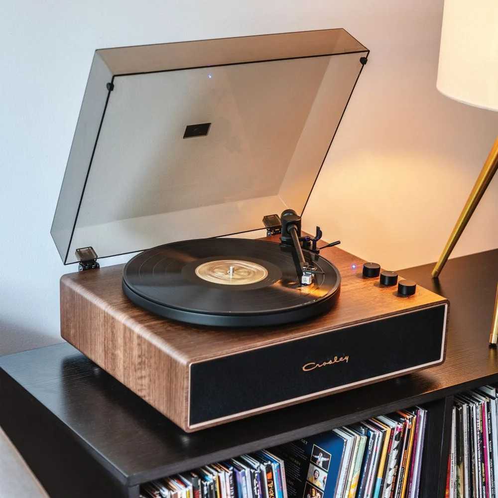 Crosley Stave Record Player - WalnutGold sits elegantly on a shelf with a lifted dust cover