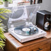 Crosley T400D Component Bluetooth Turntable - White is shown playing a record on a wooden surface with a nearby speaker and books in the background