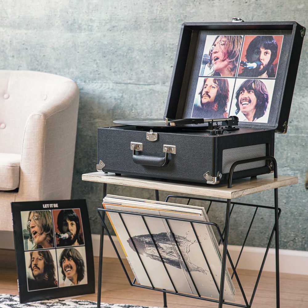 Crosley The Beatles Anthology Portable Bluetooth Turntable - Let It Be sits open on a small table, showcasing album art inside the lid, with a record rack nearby