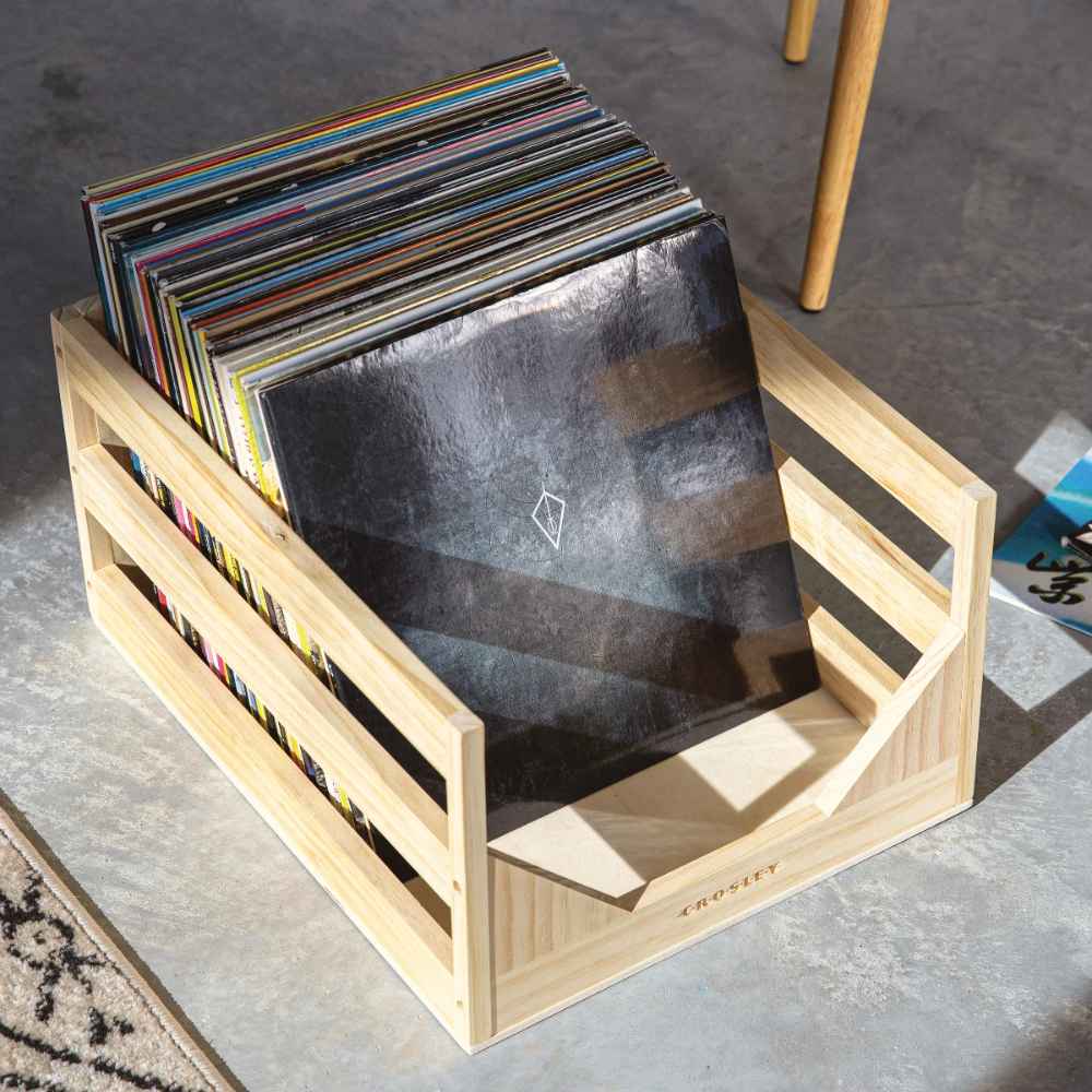 Crosley Vinyl Record Storage Crate - Natural is shown filled with colorful vinyl records in a minimal, open design on a concrete floor