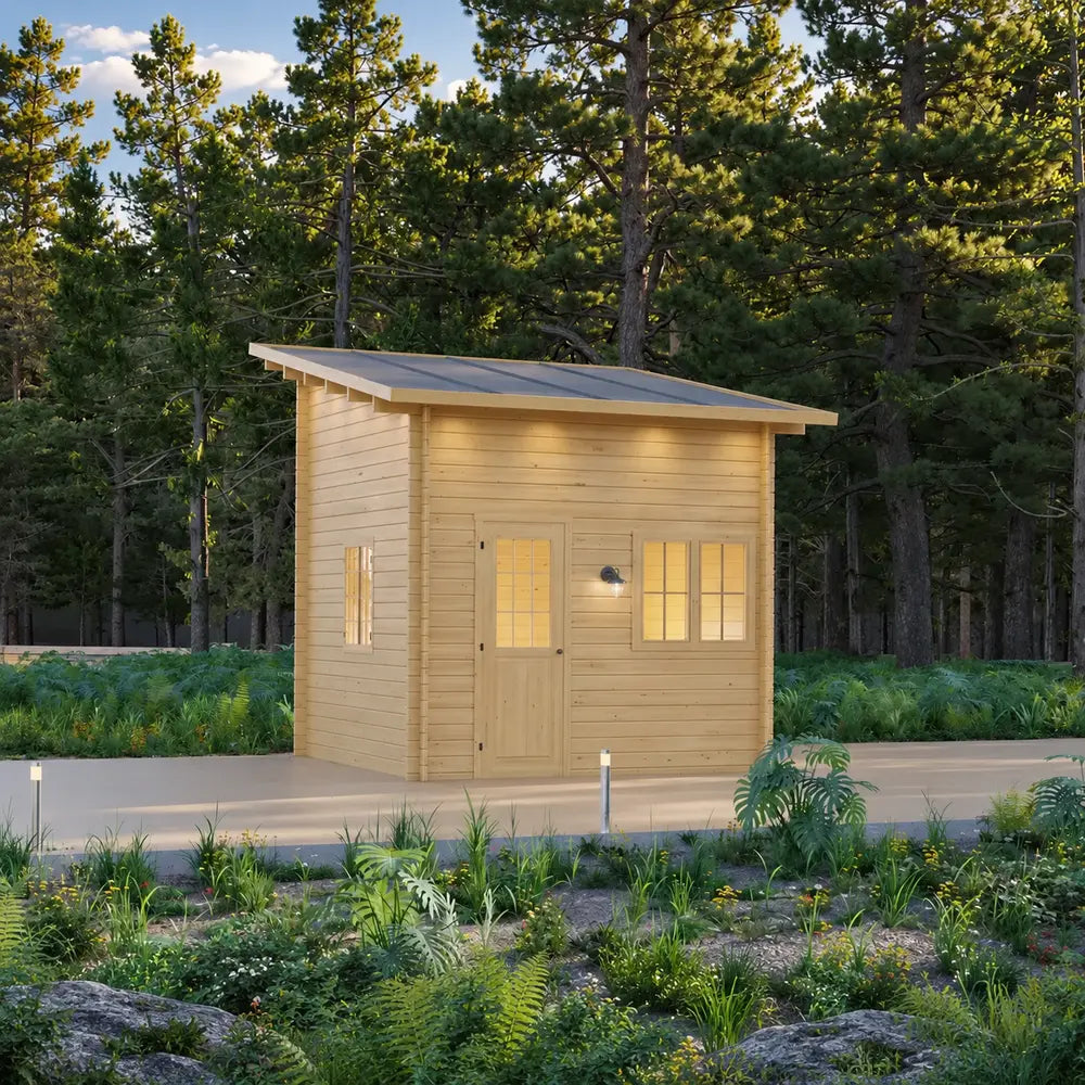 Cube Loft 100 garden room with a gray angled roof, pale wood exterior, multiple windows, glazed door, pathway lighting, and dense woodland surroundings.