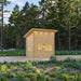 Front angled view of the Cube Loft 100 garden room with pale wood siding, a tall sloped roof, illuminated windows, modern pathway lights, and forest landscaping.