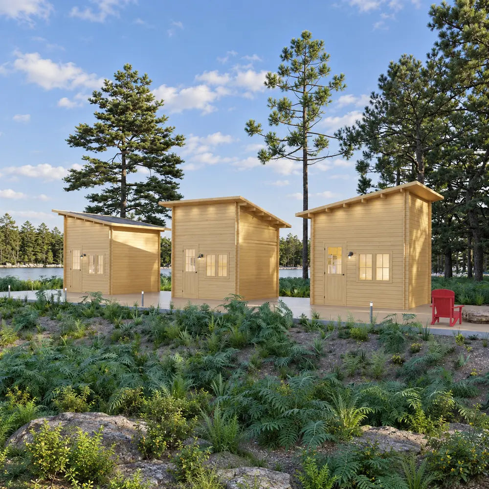 Three Cube Loft 100 garden room units arranged along a landscaped forest path beside a lake, with pale wood exteriors, sloped roofs, pathway lights, and a red Adirondack chair.