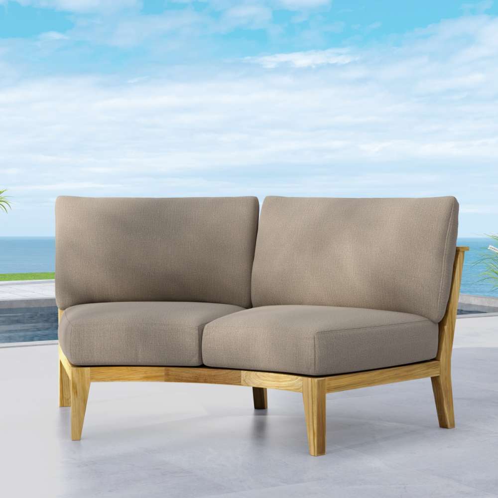 Cushioned Westminster Teak Kafelonia Sofa Sectional with a light teak frame is placed on an outdoor patio overlooking the ocean under a blue sky