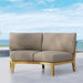 Cushioned Westminster Teak Kafelonia Sofa Sectional with a light teak frame is placed on an outdoor patio overlooking the ocean under a blue sky