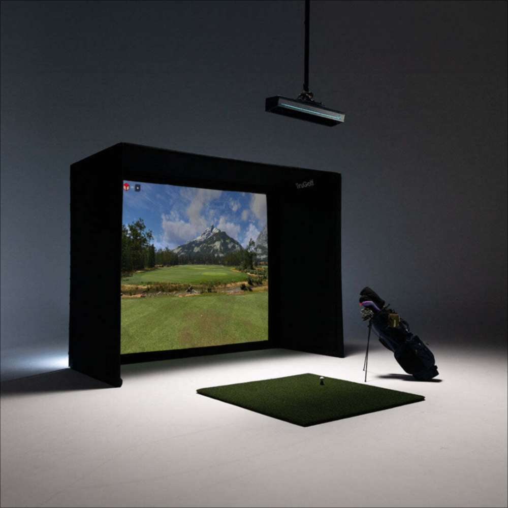 Dark room shows a virtual golf course on a large screen with a golf bag beside it powered by TruGolf APOGEE Golf Launch Monitor w/ Starter 10 (2025) Enclosure