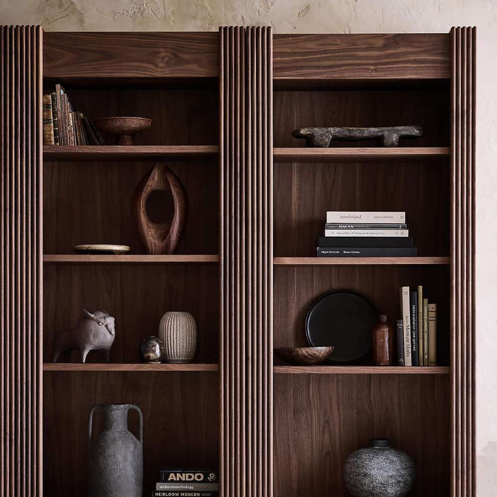 Decorative display on Crate & Barrel Siena 34" Walnut Wood 4-Shelf Storage Bookcase with Drawer showcasing books vases and sculptural accents