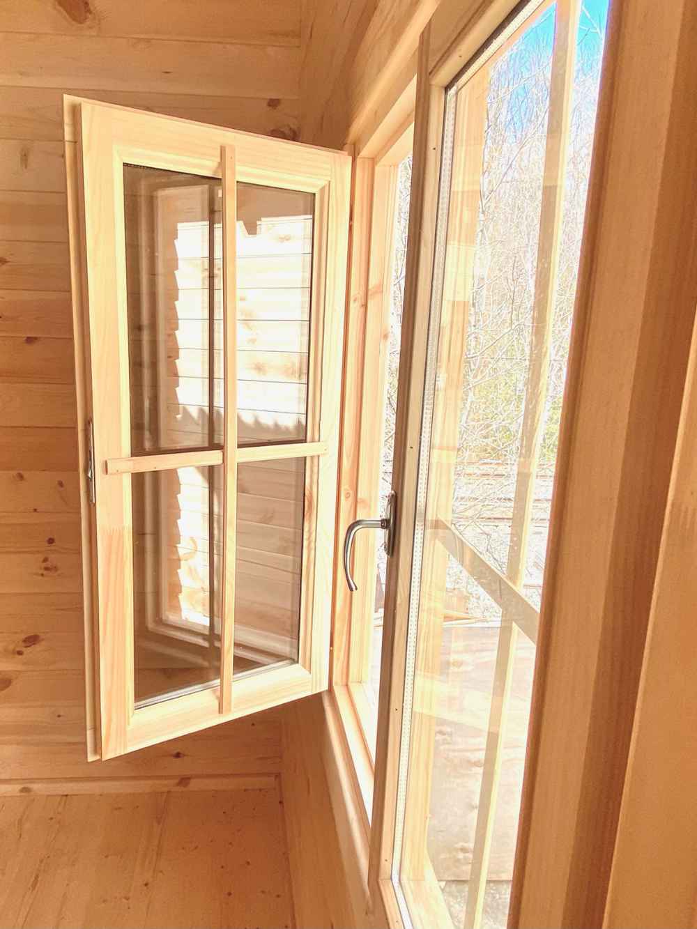 Detailed look at an open wooden-framed window letting in sunlight inside the Sawmill Structures Harvest Grand Bungalow 107 Garden Room