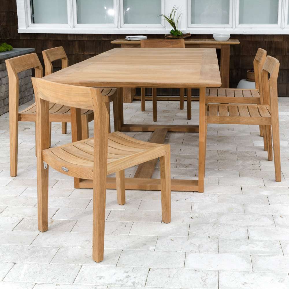 Dining set with multiple Westminster Teak Horizon Teak Side Chair units is arranged around a table on a stone patio in front of a house
