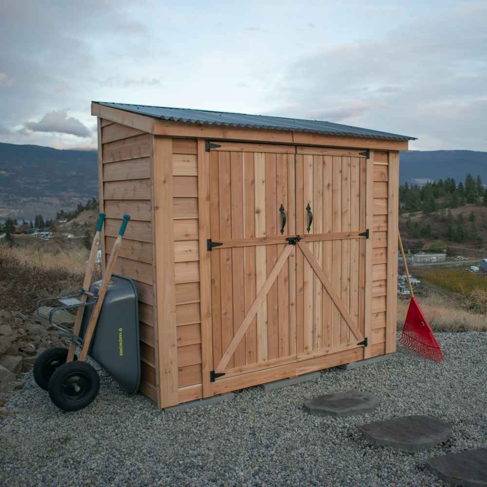 Double Door Metal Roof Outdoor Living Today 8×4 SpaceSaver Lean-To Cedar Shed stands on gravel with yard tools