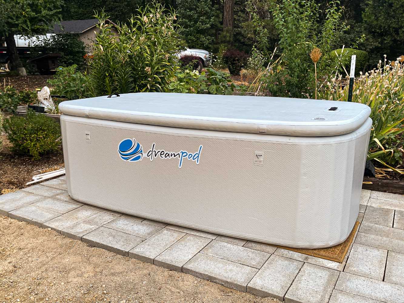 Dreampod Home Float FLEX positioned on a tiled patio surrounded by a natural garden with a fitted cover on top for protection