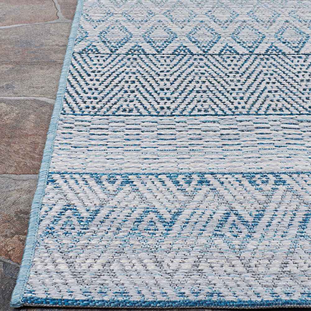Edge of the Couristan Cape Indoor/Outdoor Rug - Gables/Surf is shown resting on a stone floor