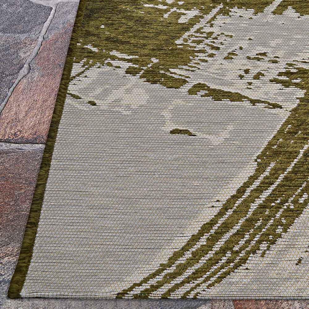 Edge of the Couristan Castille Indoor/Outdoor Rug - Canvas/Tea Leaf rests on stone pavers