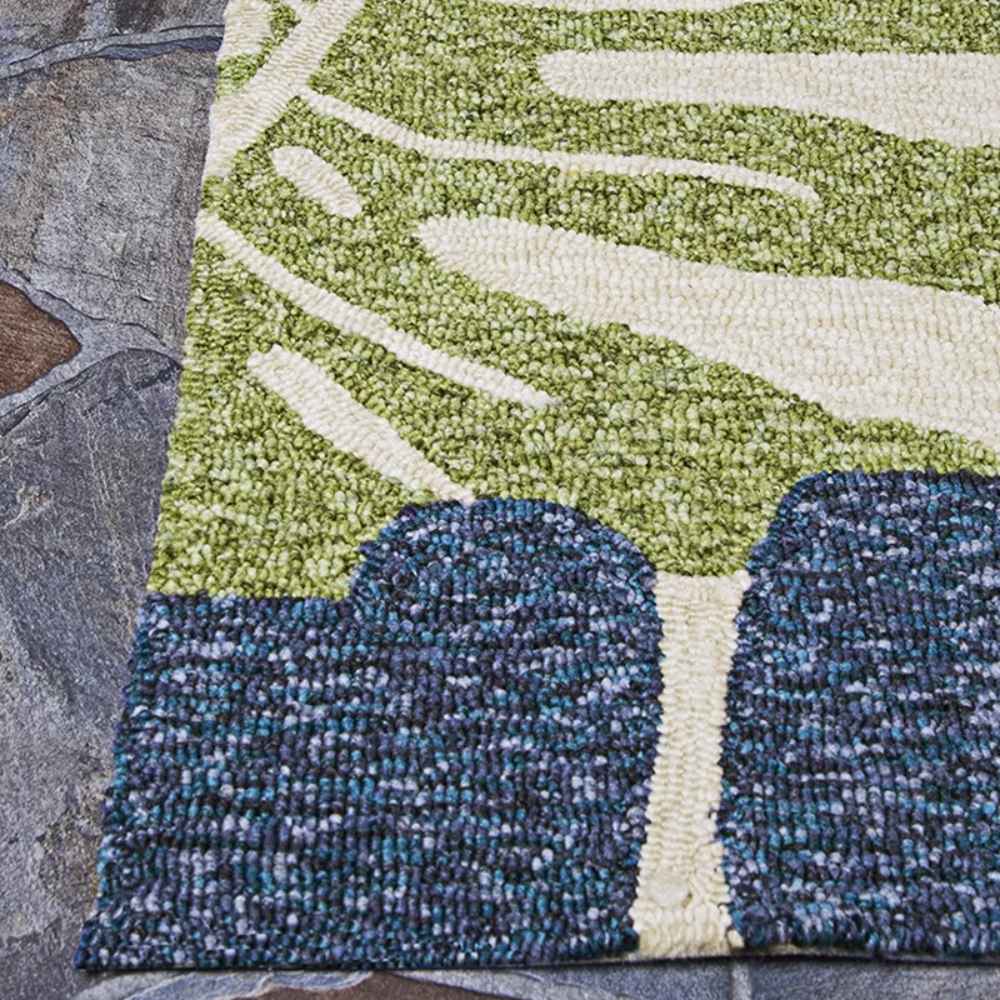 Edge of the Couristan Covington Indoor/Outdoor Rug - Monstera/Cream-Multi is shown lying flat on a slate patio, highlighting its clean finish