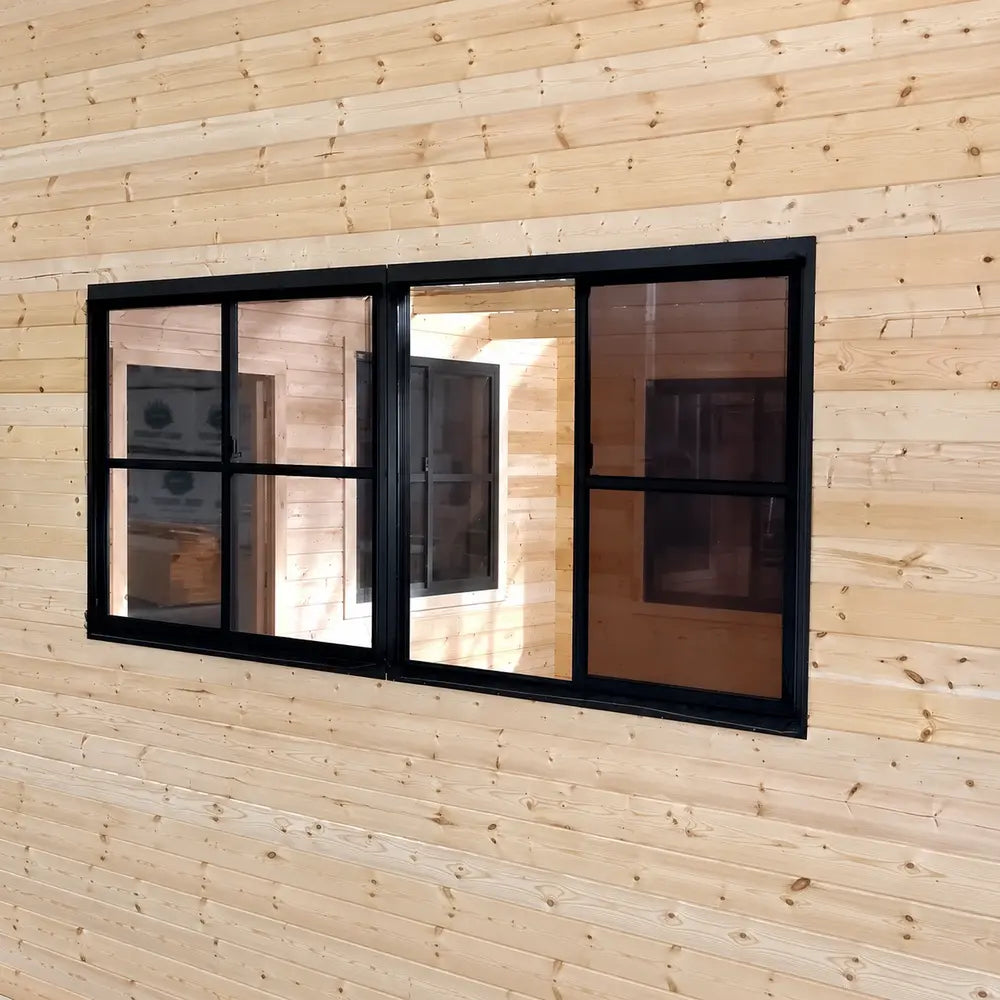 Straight interior view of a large black-framed Eze-Breeze sliding-window system installed in a pale pine wall, showing multiple sliding panels and an adjoining wooden room.
