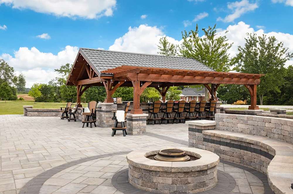 Fire pit area near Brookside Timber Frame Combolan Estate Pavilion adds a cozy gathering spot, surrounded by curved stone seating and scenic outdoor beauty