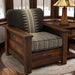 Fireside Lodge Barnwood Americana Lounge Chair is pictured in a cozy cabin-style room, showcasing its rustic wood frame and patterned cushions beside a craftsman-style lamp