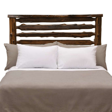 Fireside Lodge Cedar Log Headwaters Headboard shows the cedar log headboard attached to a bed with a dark rustic finish