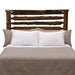 Fireside Lodge Cedar Log Headwaters Headboard shows the cedar log headboard attached to a bed with a dark rustic finish