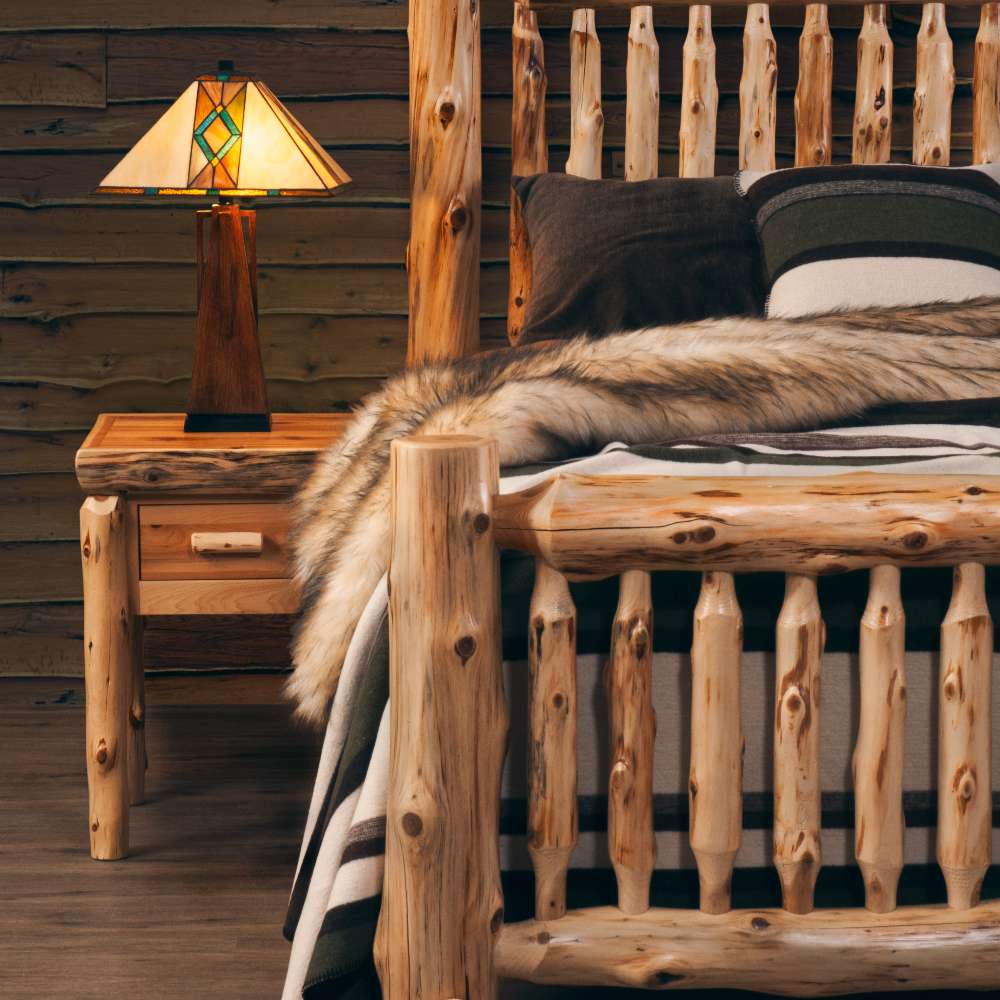 Fireside Lodge Cedar Log Small Spindle Bed is pictured in a cabin-style setting, showing thick cedar posts, spindle details, and a nightstand beside it