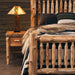 Fireside Lodge Cedar Log Small Spindle Bed is pictured in a cabin-style setting, showing thick cedar posts, spindle details, and a nightstand beside it