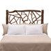 Fireside Lodge Hickory Log Twig Headboard features a rustic log frame with intertwined twig details behind a bed with light neutral bedding
