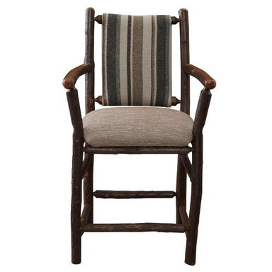 Fireside Lodge Hickory Log Upholstered Counter Stool with Arms features a solid log frame, rounded wooden arms, a padded beige seat, and a vertically striped upholstered back