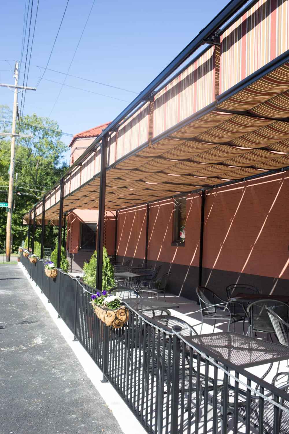 Flower planters and metal railings border a sunlit patio shaded by the stylish Structureworks Silhouette Aluminum Patio Cover & Pergola