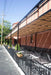 Flower planters and metal railings border a sunlit patio shaded by the stylish Structureworks Silhouette Aluminum Patio Cover & Pergola