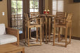 Four tall wooden chairs surround a high table indoors near glass doors, with drinks on top, showcasing the Westminster Teak Somerset Teak Bar Stool in a cozy home setting