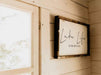 Framed wall sign that reads “Lake Life is the Best Life” next to a wooden-framed window inside the Sawmill Structures Harvest Grand Bungalow 107 Garden Room