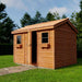 From a diagonal view, the Outdoor Living Today Large 12×8 Cabana Garden Shed showcases its wooden single siding, cedar roof, two square windows with flower boxes, and a gently sloped shingle roof
