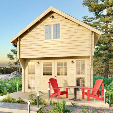 Front-facing view of the Sawmill Structures Grand Loft 107 Deluxe DD Garden Room shows its wood construction, large loft window, and red chairs arranged on the patio