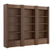 Front view of Crate & Barrel Siena 102" Walnut Wood 4-Shelf Storage Bookcase with Drawer, Set of 3 with decorative fluted sides, open shelves, and lower drawers styled with books and vases