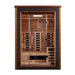 Front view of Golden Designs Nora 2 Person Outdoor-Indoor PureTech Hybrid Full Spectrum Sauna showing a dark exterior, glass door, carbon panels and a guarded stove beside the bench