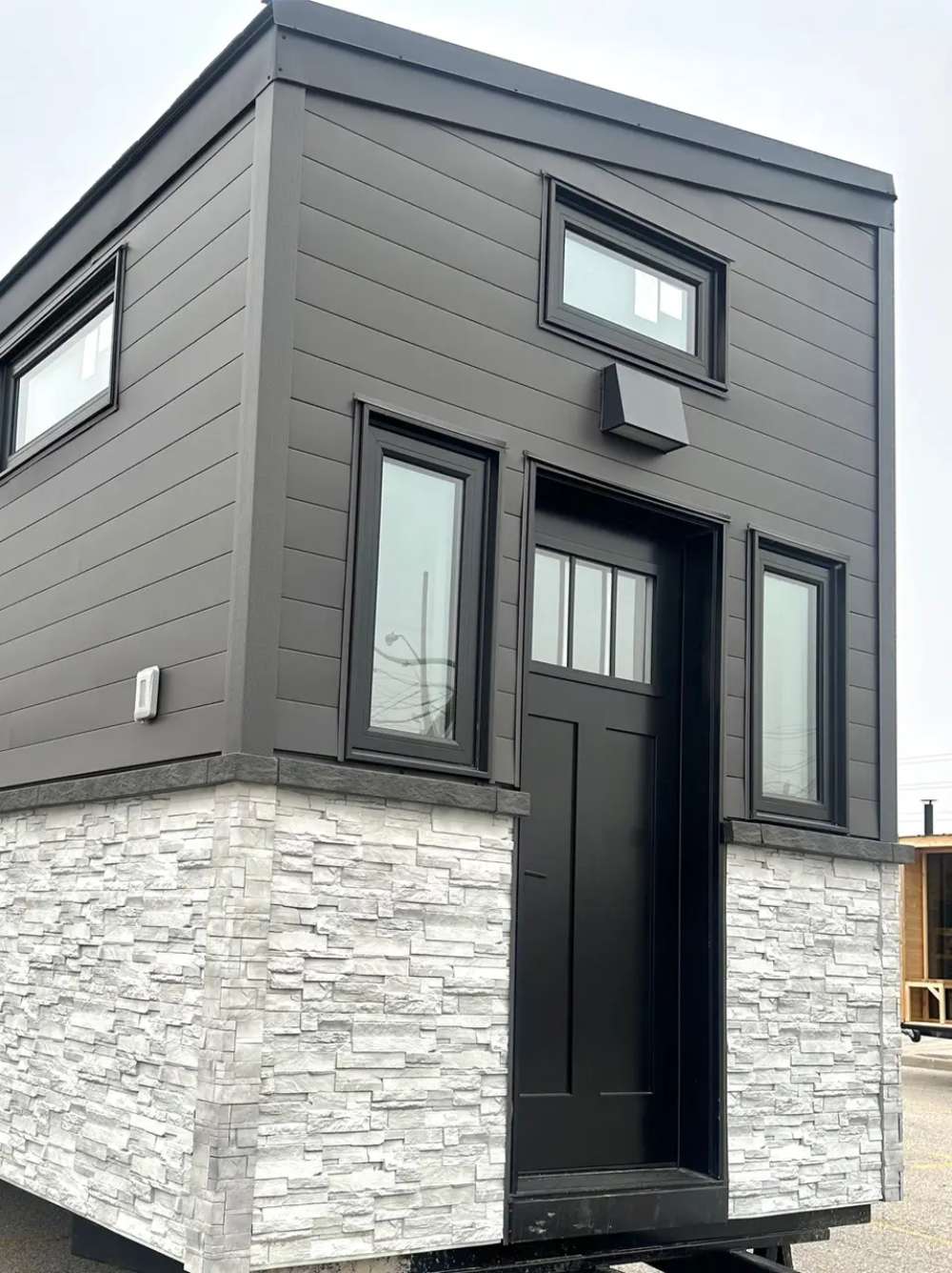 Front view of Sawmill Structures Wanderlove Tiny Home showcases a tall black entry door framed by narrow windows and a transom window above