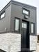 Front view of Sawmill Structures Wanderlove Tiny Home showcases a tall black entry door framed by narrow windows and a transom window above