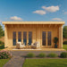 Front view of the GardenHouse24 USA Arhus 70 Garden Room shows a modern wooden cabin with large glass doors and a cozy porch setup with two chairs and a small table