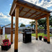Full backyard view shows Outdoor Living Today Western Red Cedar 8x5 Grill Gazebo with flowers, fencing, and a grill underneath