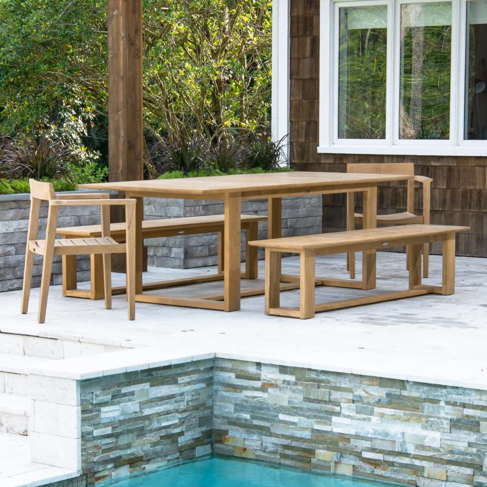 Full outdoor patio setup shows Westminster Teak Horizon Table & Bench Set with benches and chairs placed beside a pool and greenery