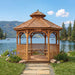 Full outdoor view of Outdoor Living Today Western Red Cedar Octagon Bayside Gazebo surrounded by flowers, grass, and a lakefront setting